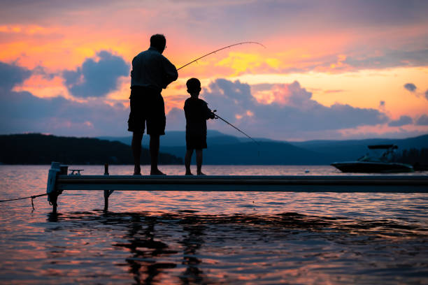 A grandfather and grandson fishing together from a jetty at dusk